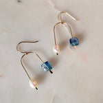 Load image into Gallery viewer, Pair of asymmetric arch gold fill earrings with kyanite beads, and pearls on a textured beige background.
