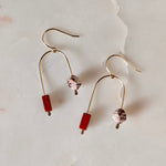 Load image into Gallery viewer, Pair of asymmetric arch gold fill earrings with red jasper beads, and faceted Venus jasper beads on a textured beige background.
