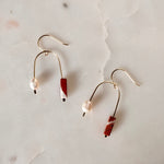 Load image into Gallery viewer, Pair of asymmetric arch gold fill earrings with red and white jasper beads, and pearls on a textured beige background.
